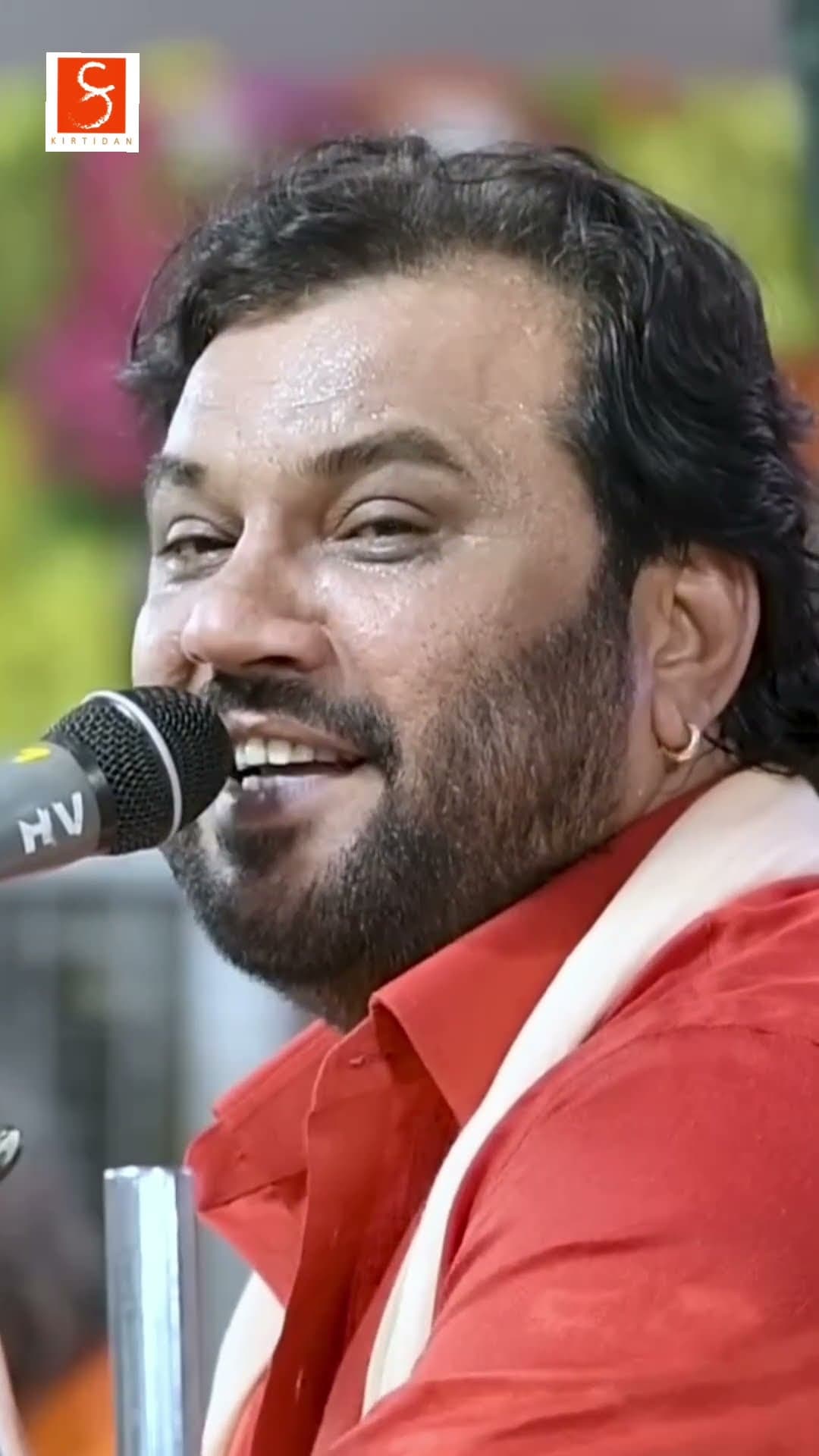 Kirtidan Gadhvi smiling as he sings into a microphone, in a red kurta