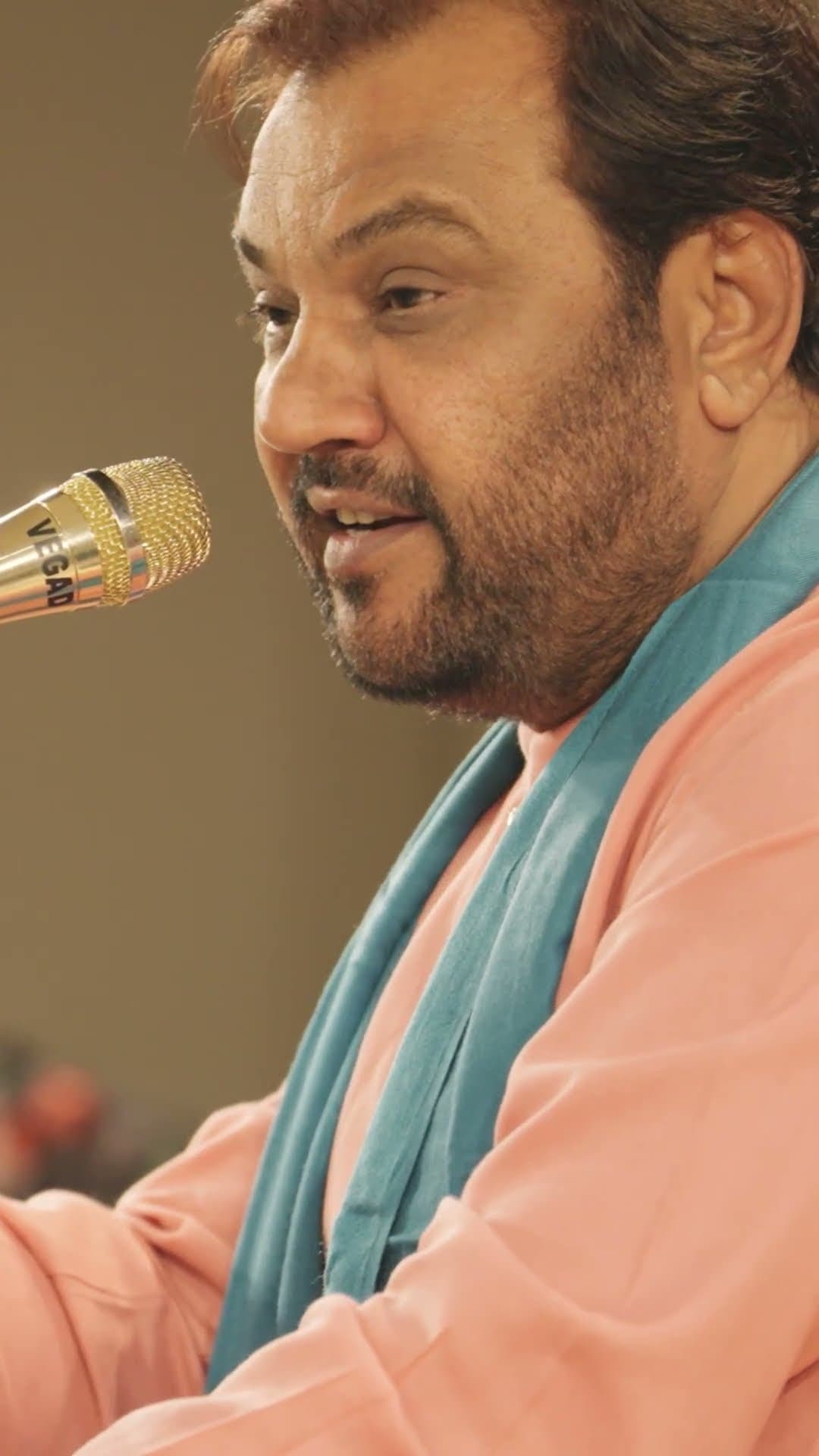 Kirtidan Gadhvi singing in profile, in a peach kurta with a teal scarf