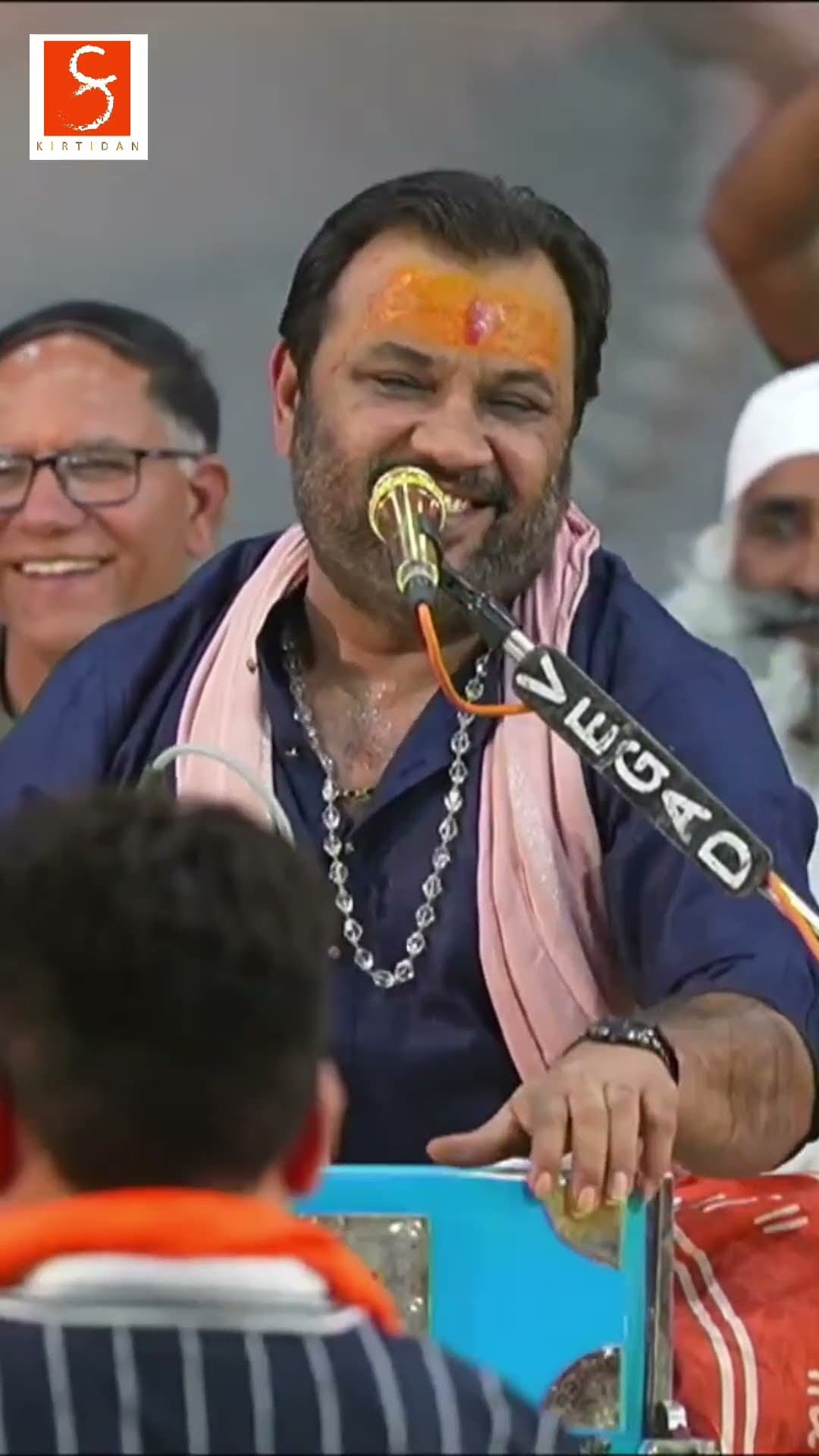 Kirtidan Gadhvi singing at the harmonium during a dayro, with a saffron scarf